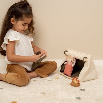 Criança a brincar com brinquedos de pelúcia junto a uma tenda de tecido e tapete branco