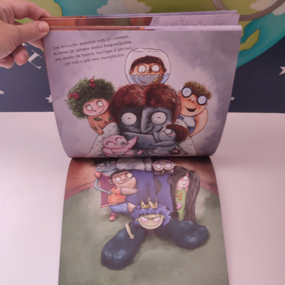 Livro infantil aberto com ilustrações coloridas de monstros e texto em português europeu.