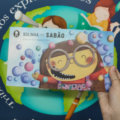 Capa de livro infantil com ilustração de menina com óculos grandes e bolas de sabão coloridas
