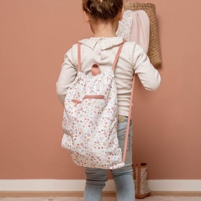 Mochila infantil branca com flores coloridas e alças rosa usada por criança em ambiente bege