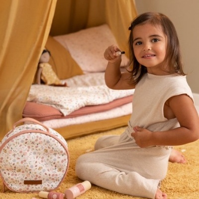 Menina a brincar com maquilhagem de brinquedo junto a mochila floral num quarto com cama e dossel amarelo