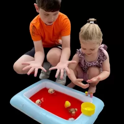 Duas crianças brincam com piscina insuflável azul claro com água vermelha e brinquedos flutuantes.