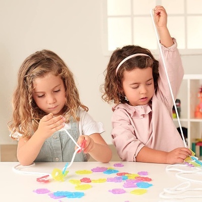 Duas meninas a jogar com peças coloridas e fios numa mesa branca