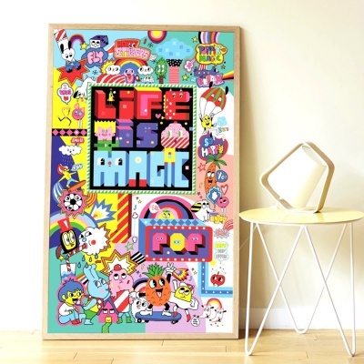 Poster colorido com texto LIFE IS MAGIC e várias ilustrações, encostado a parede, ao lado de mesa amarela com objeto decorativo