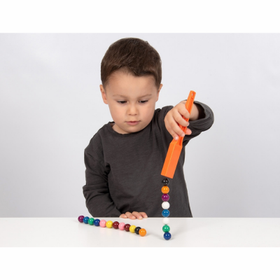 Criança a usar íman laranja para atrair bolas coloridas numa superfície branca
