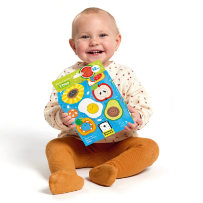 Criança segurando caixa azul com imagens de comida para crianças, vestindo collants castanhos e camisola creme com pontos vermelhos.