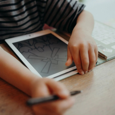 Tablet digital branco com desenho de relógio na tela e criança interagindo com ele numa mesa de madeira