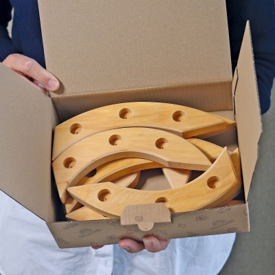 Peças curvas de madeira clara com buracos dentro de uma caixa de cartão
