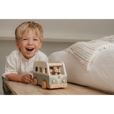 Criança a brincar com carrinha de brinquedo de madeira ao lado de cama com manta às riscas