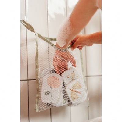 Saco de rede com sabonetes sólidos decorados, pendurado em azulejo branco com mão espumada