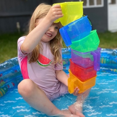 Menina na piscina insuflável a empilhar copos coloridos com água