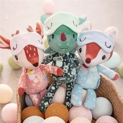 Três bonecos de pelúcia com pijamas coloridos e máscaras de dormir sentados numa cesta com bolas de tecido.