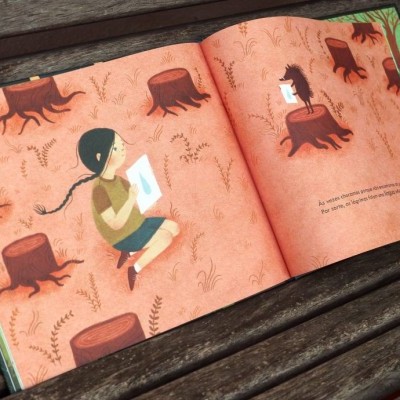 Livro ilustrado aberto num banco de madeira escura com ripas horizontais