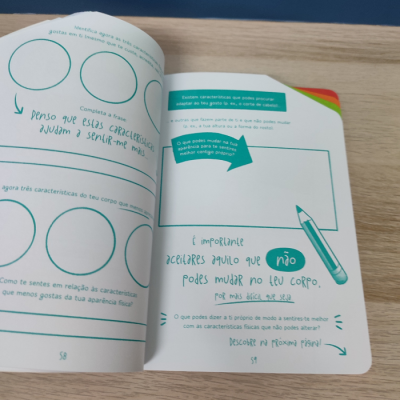 Livro aberto com texto em português europeu, círculos, setas e desenho de lápis em fundo branco sobre mesa de madeira