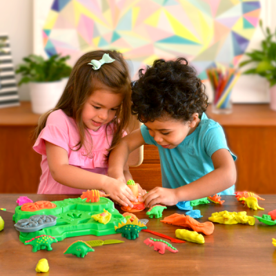 Crianças a brincar com massa moldável colorida e moldes de dinossauros.