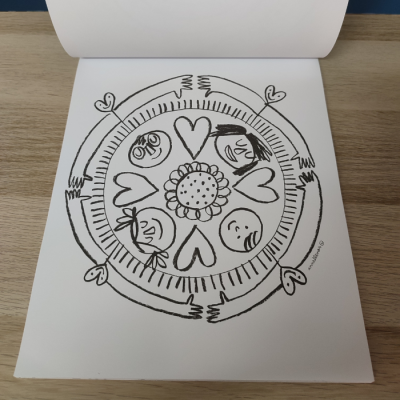 Desenho circular a preto com rostos, corações e braços numa folha branca sobre mesa de madeira