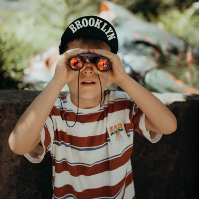 Criança com boné Brooklyn e camisa riscada a usar binóculos