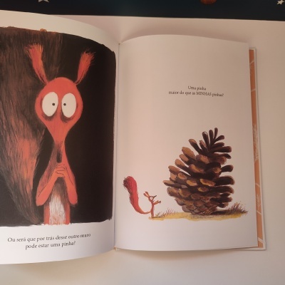 Livro aberto com ilustrações de esquilos e uma pinha grande, texto em português nas páginas.