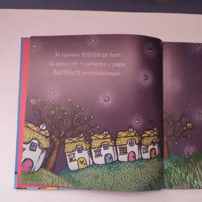 Livro infantil ilustrado com casas, árvores e texto em português no céu noturno