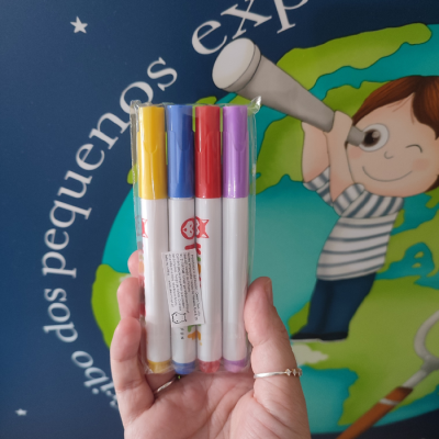 Quatro marcadores coloridos em embalagem transparente segurados à frente de ilustração de criança com telescópio.