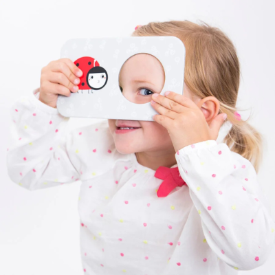 Criança usa um espelho redondo integrado numa placa branca com joaninha desenhada