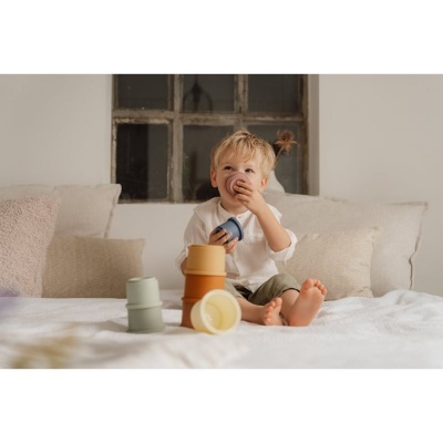 Criança a brincar com copos de empilhar em cama com almofadas e janela atrás