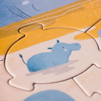 Peça de puzzle de madeira com desenho de hipopótamo azul sobre fundo bege, amarelo e azul