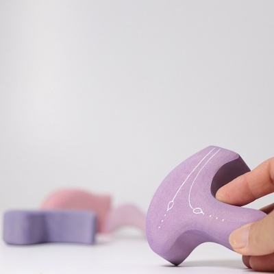 Brinquedo moldável roxo com padrões brancos segurado por uma mão, fundo com objetos similares desfocados