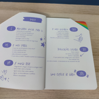 Livro aberto com índice em português e abas coloridas, sobre mesa de madeira