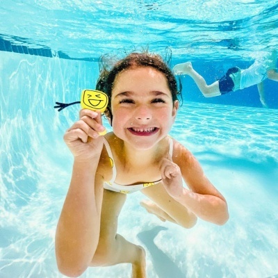 Criança na piscina a segurar brinquedo amarelo com rosto sorridente.