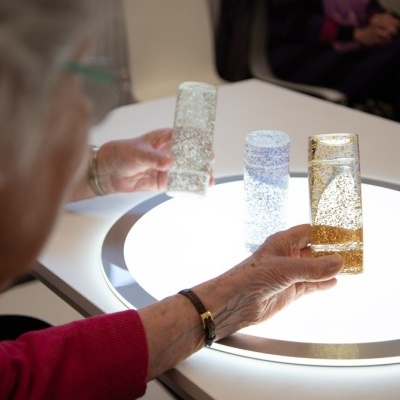 Pessoa segurando copos de vidro decorativos sobre superfície iluminada branca