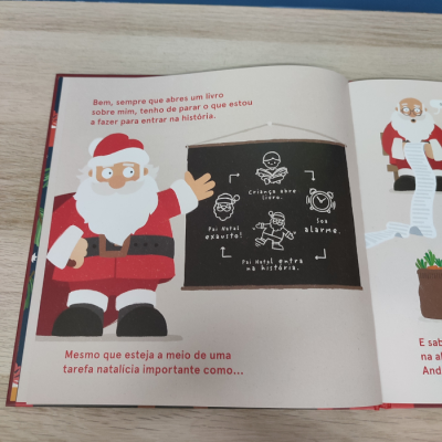 Livro ilustrado aberto com Pai Natal, texto e quadro-negro desenhado com instruções em português.