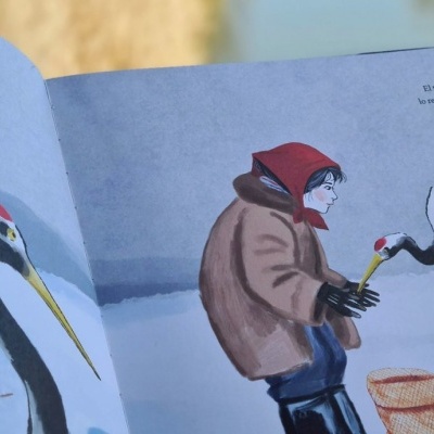 Página aberta de livro ilustrado com uma pessoa e cegonhas em fundo de neve