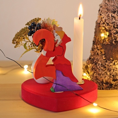 Figurine em madeira colorida com vela acesa numa base vermelha em forma de coração.