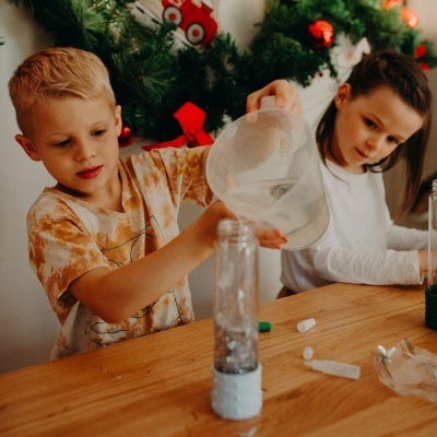 Crianças a manusear garrafas transparentes na mesa de madeira com decoração natalícia ao fundo