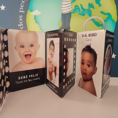 Livro de bebé com fotos e textos em português, fundo com mapa e estrelas.