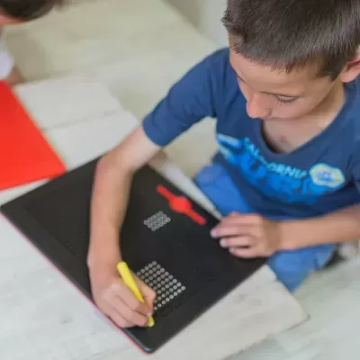 Caderno preto com elementos vermelhos e amarelo usado por criança em mesa clara