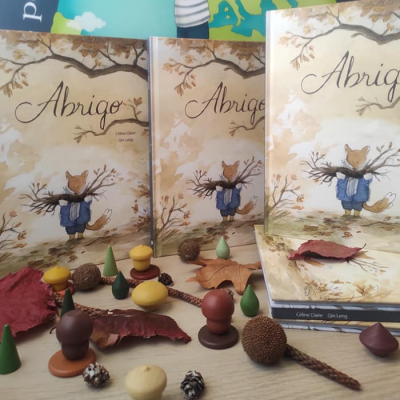 Livros infantis 'Abrigo' com ilustração de raposa e objetos naturais numa mesa