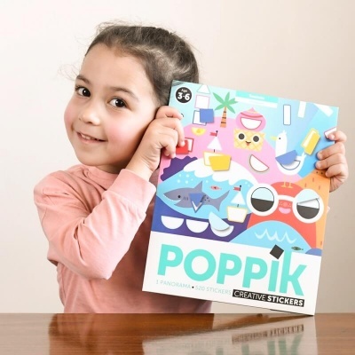 Caderno de stickers Poppik colorido segurado por criança junto a mesa