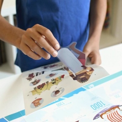 Pessoa destacando figurinha colorida de folha sobre mesa branca