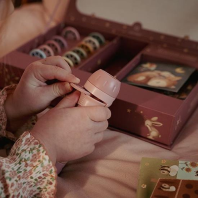 Mãos com carimbo rosa claro e caixa de carimbos decorada com estrelas e coelhinhos