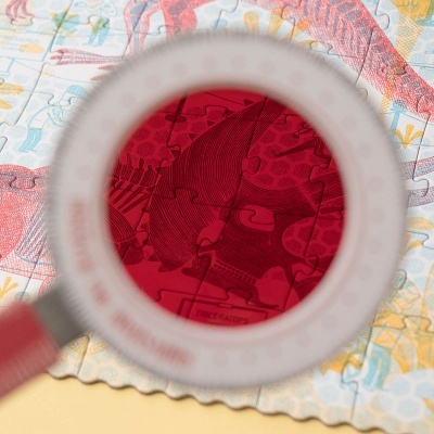 Lupa com lente vermelha sobre peça de puzzle vermelha e colorida.