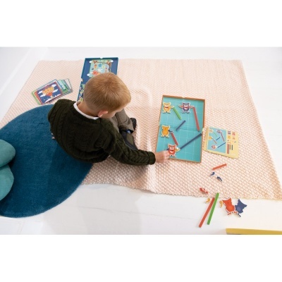 Criança a jogar jogo de tabuleiro com peças coloridas e cartões num tapete bege