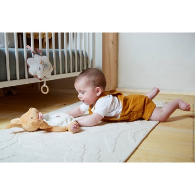 Bebé deitado a brincar com peluche num tapete branco em quarto com berço.