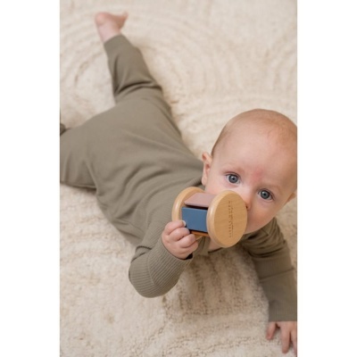 Bebé deitado com macacão verde-acinzentado segurando brinquedo de madeira.