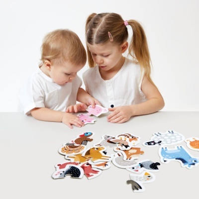 Duas crianças montando um puzzle de animais coloridos numa mesa branca