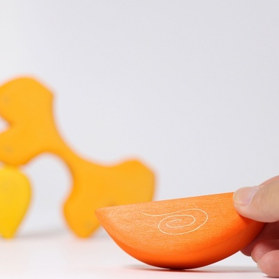 Peça de brinquedo de madeira laranja com padrão em espiral e outras peças coloridas ao fundo