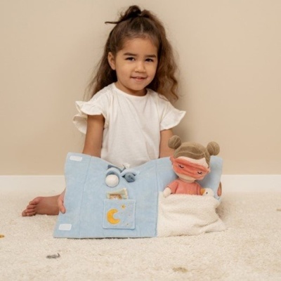 Menina com livro de tecido azul e boneca de pano num tapete bege