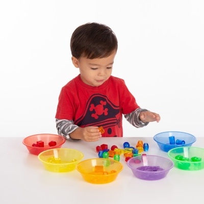 Criança com copos coloridos e peças pequenas sobre mesa branca