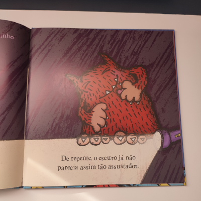 Página de livro infantil com ilustração de monstro vermelho e texto em português europeu.
